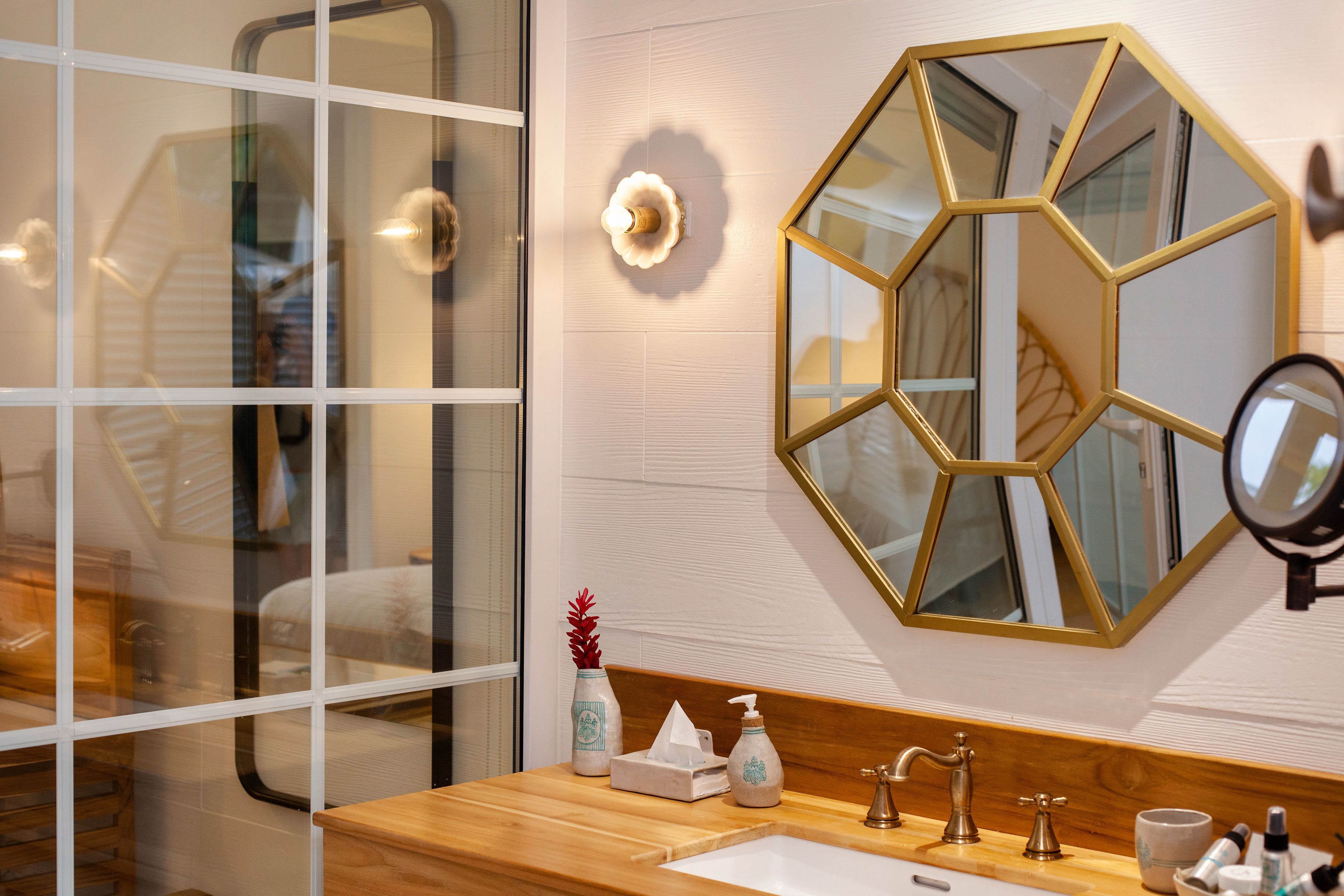 Ein Badezimmer mit einem Holzkosmetikschrank, einem großen Spiegel, einer geometrischen Wanddekoration und einem Fenster mit Blick ins Innere.