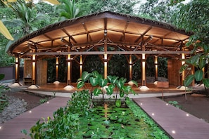 A wooden pavilion with a thatched roof, surrounded by a garden with water lilies and tropical plants. - Hotel Aguas Claras Member of the Cayuga Collection (Cahuita)