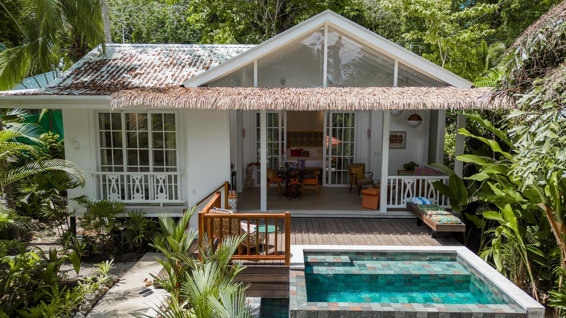 Ein zweigeschossiges Haus mit Strohdach, Pool und einer Terrassenanlage.