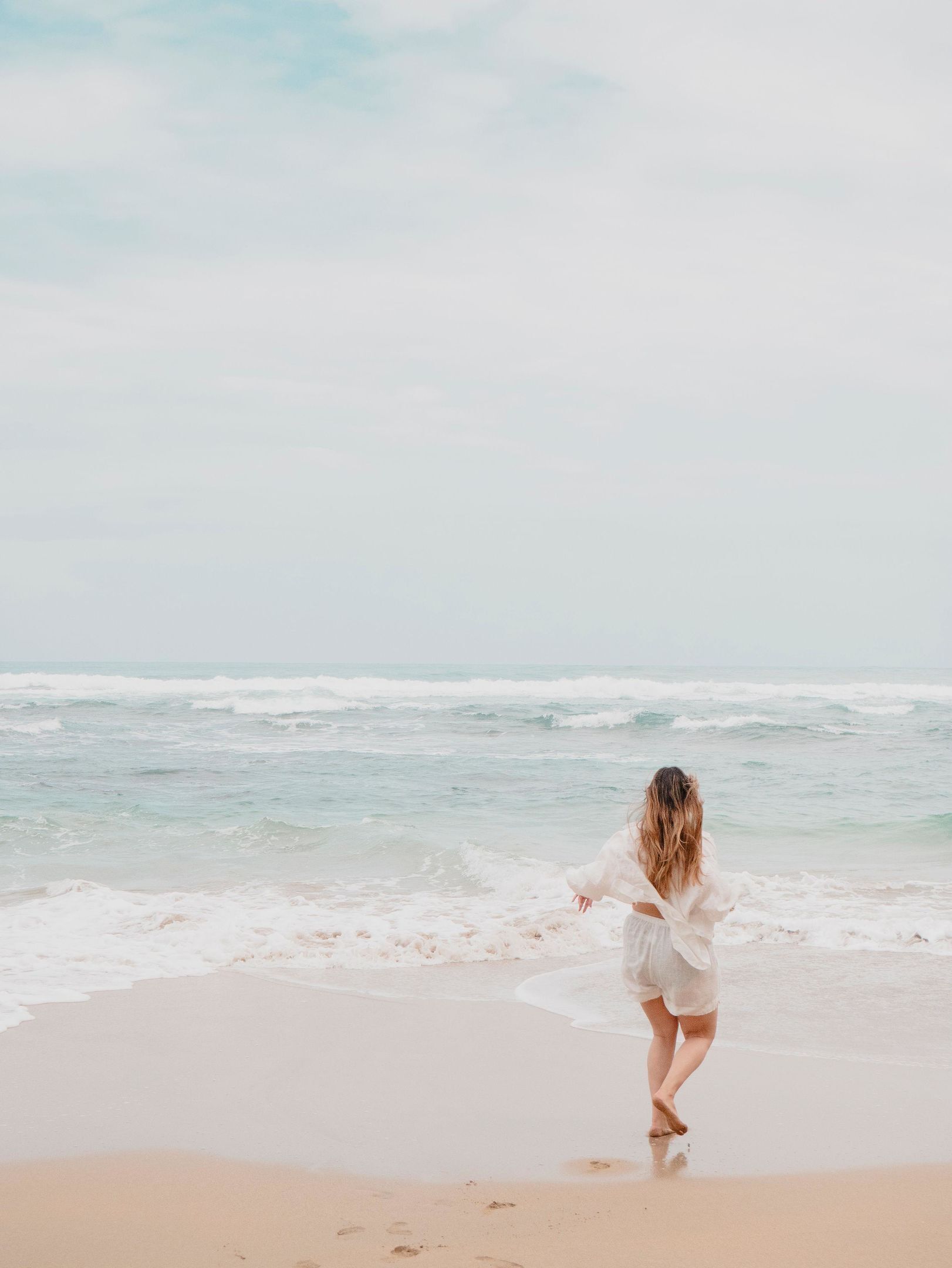 A person walking on a beach with waves in the background.