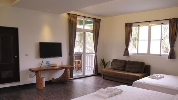 Ein Hotelzimmer mit zwei Betten, einem Fernseher, einem Holztisch, einer Couch und einem Balkon mit Vorhängen.
