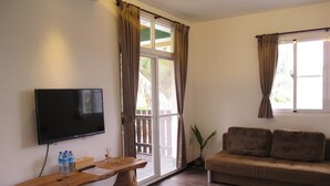 Ein Wohnzimmer mit Flachbildfernseher, Holztisch, Sofa und einer Glastür zum Außenbereich.