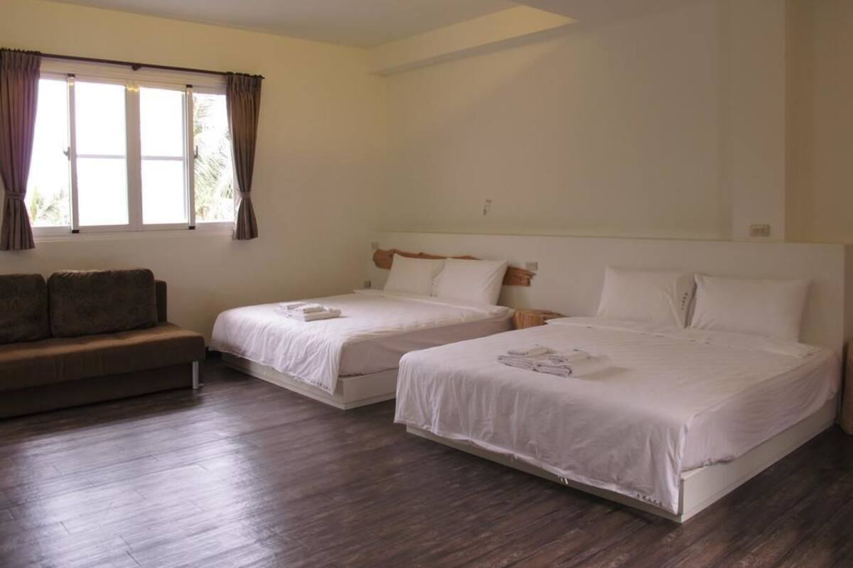Habitació d'hotel amb dos llits, un sofà i una finestra gran amb cortines.