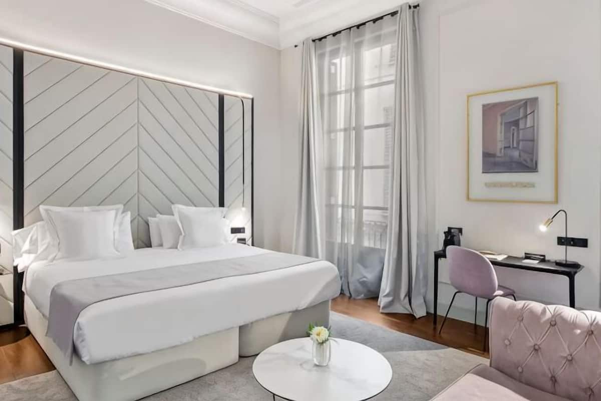 Moderni hotellihuone, jossa on suuri sänky, työpöytä, tuoli ja näkymä kaupunkiin.