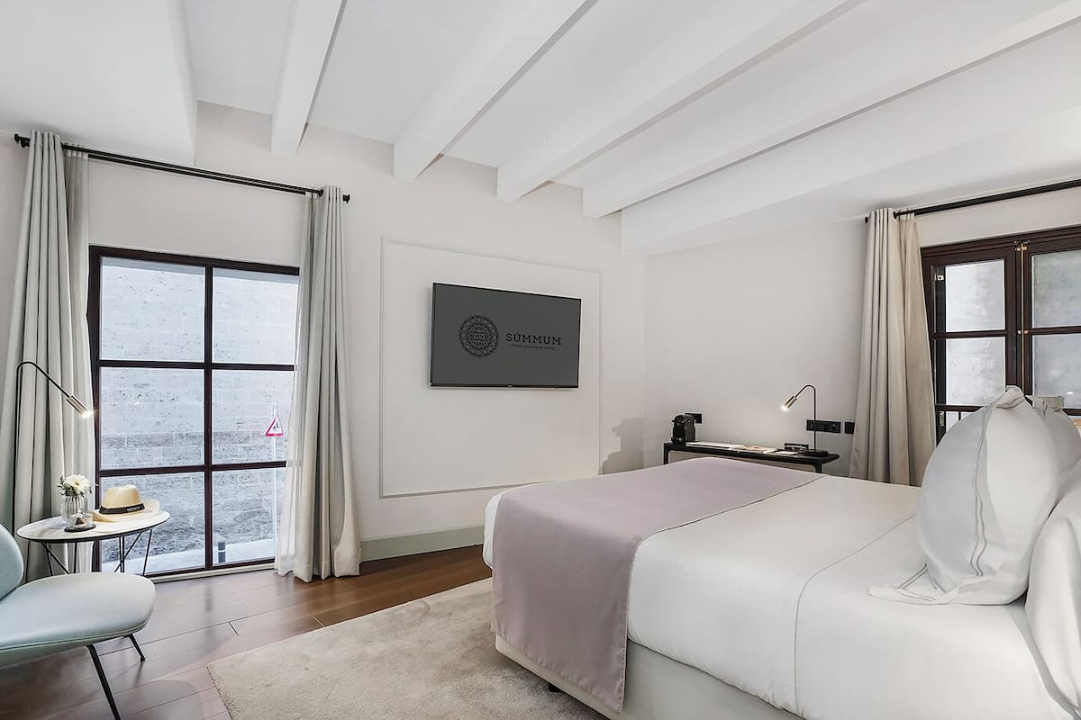 A modern hotel room with a large bed, a desk, and a view through large windows.