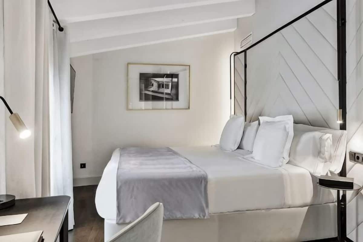 A bedroom with a bed, bedside table, lamp, and a framed picture on the wall.