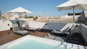 Un área de piscina en la azotea con sillas de descanso y sombrillas, con vista a un paisaje urbano.