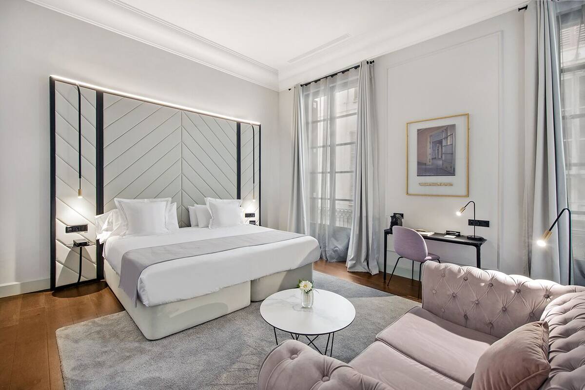 A modern hotel room with a large bed, a desk, a chair, and a sofa.