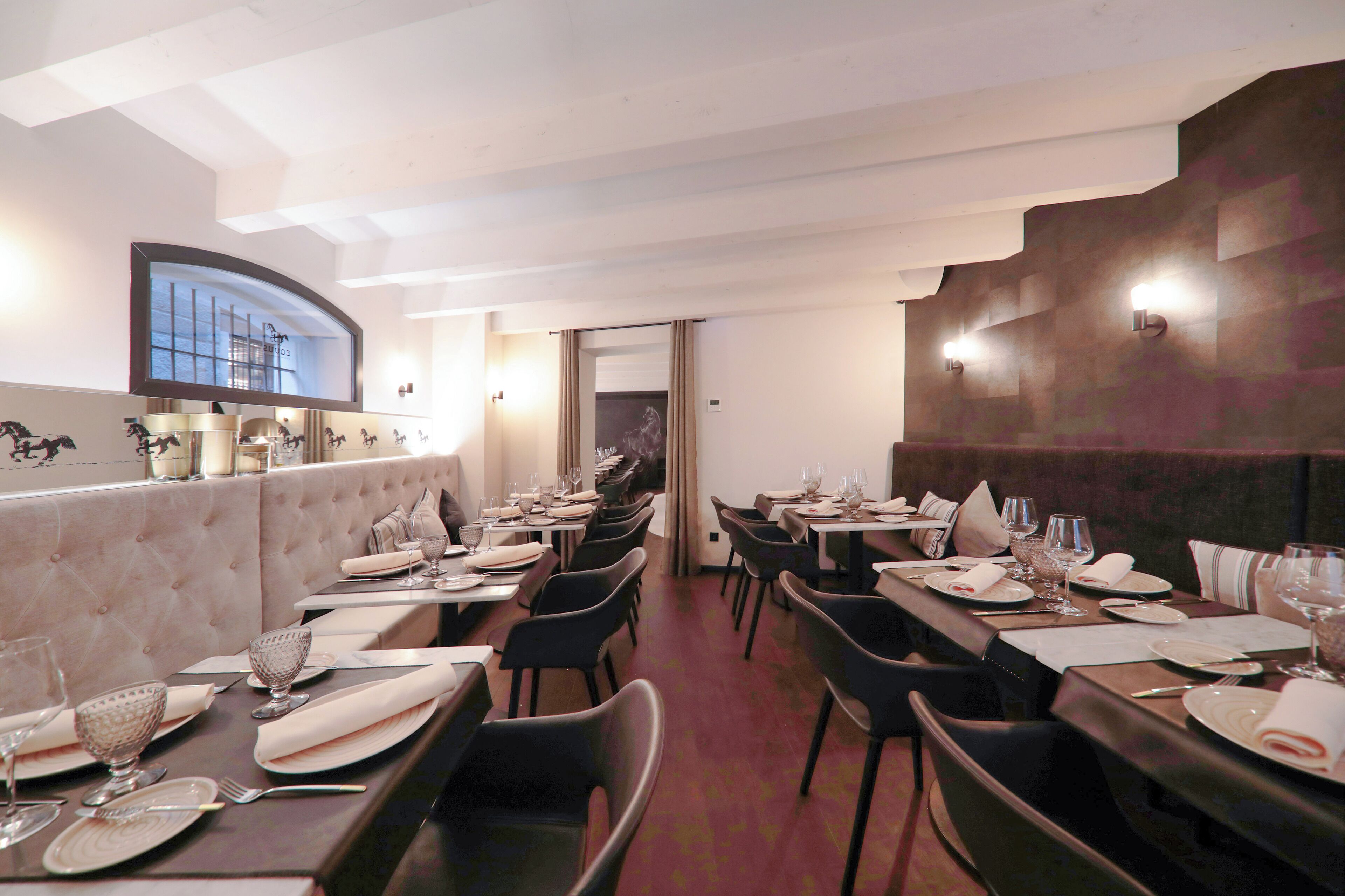 Un restaurante con un comedor largo y elegante, techo alto y vista al cielo a través de un gran ventanal. Las mesas están impecablemente dispuestas con vajilla fina, copas y sillas negras.