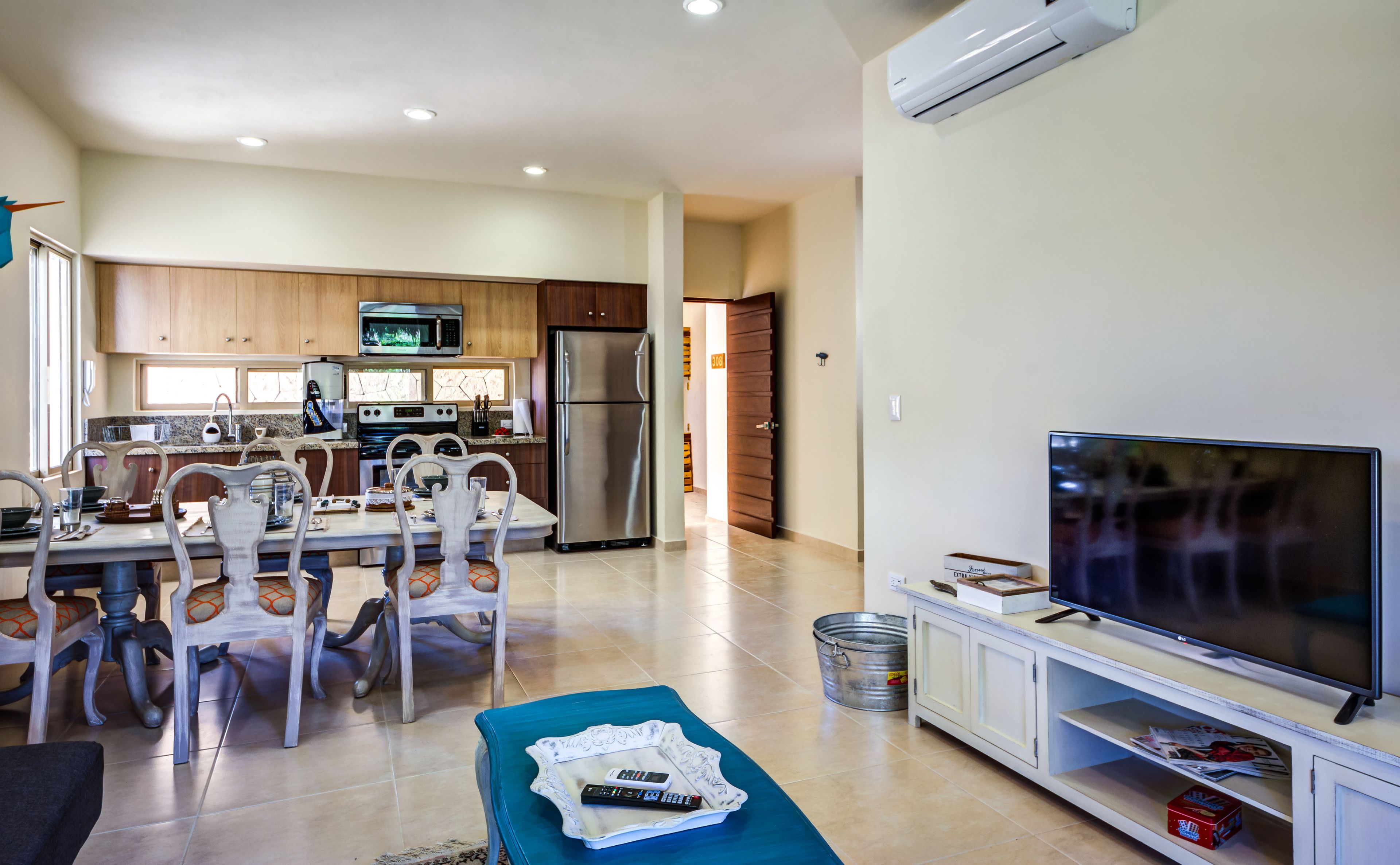 A modern kitchen with stainless steel appliances, a dining area with white chairs, and a flat-screen TV on a white stand.