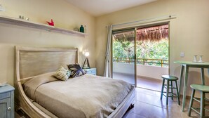 A bedroom with a bed, bedside table, and a balcony with a view of greenery.