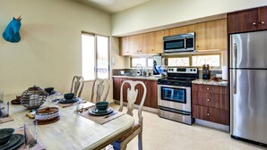A modern kitchen with wooden cabinets, stainless steel appliances, and a dining area with a table set for four.