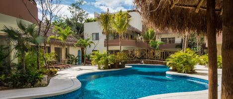 A pool area with a curved design, surrounded by lounge chairs and tropical plants.