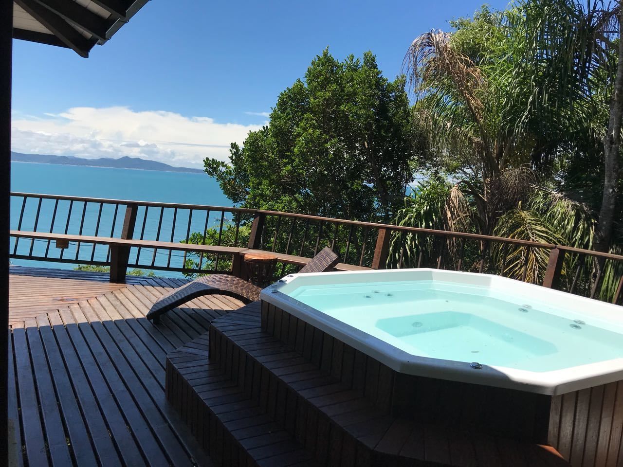 Una terraza de madera con un jacuzzi, mobiliario exterior y vista al océano.