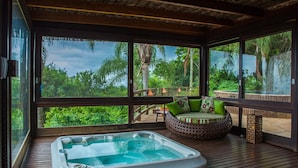 A hot tub on a wooden deck with a view of lush greenery and a wooden deck with a sofa and cushions. - Refúgio do Estaleiro (Porto Belo)