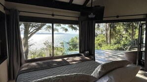 A bedroom with a large bed, a view of the sea, and a balcony with a wicker chair. - Refúgio do Estaleiro (Porto Belo)