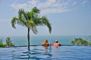 A couple relaxing in a infinity pool with a view of the sea and a palm tree. - Refúgio do Estaleiro (Porto Belo)