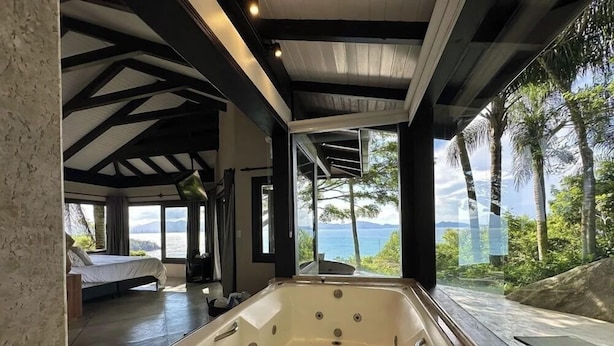 A modern bathroom with a large bathtub, a shower area, and a view of the sea. - Refúgio do Estaleiro (Porto Belo)