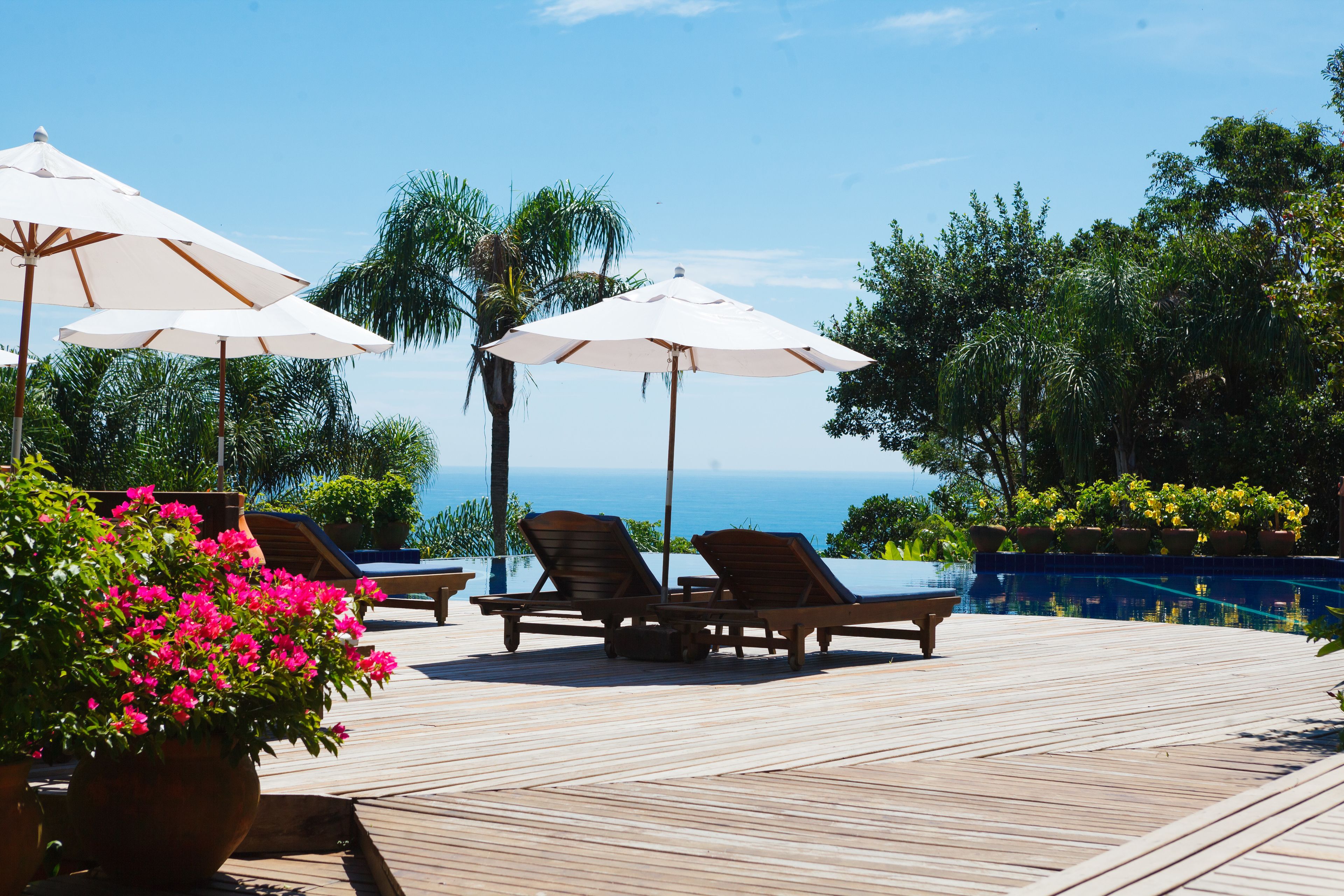 A wooden deck with lounge chairs and umbrellas overlooking a swimming pool and the ocean.