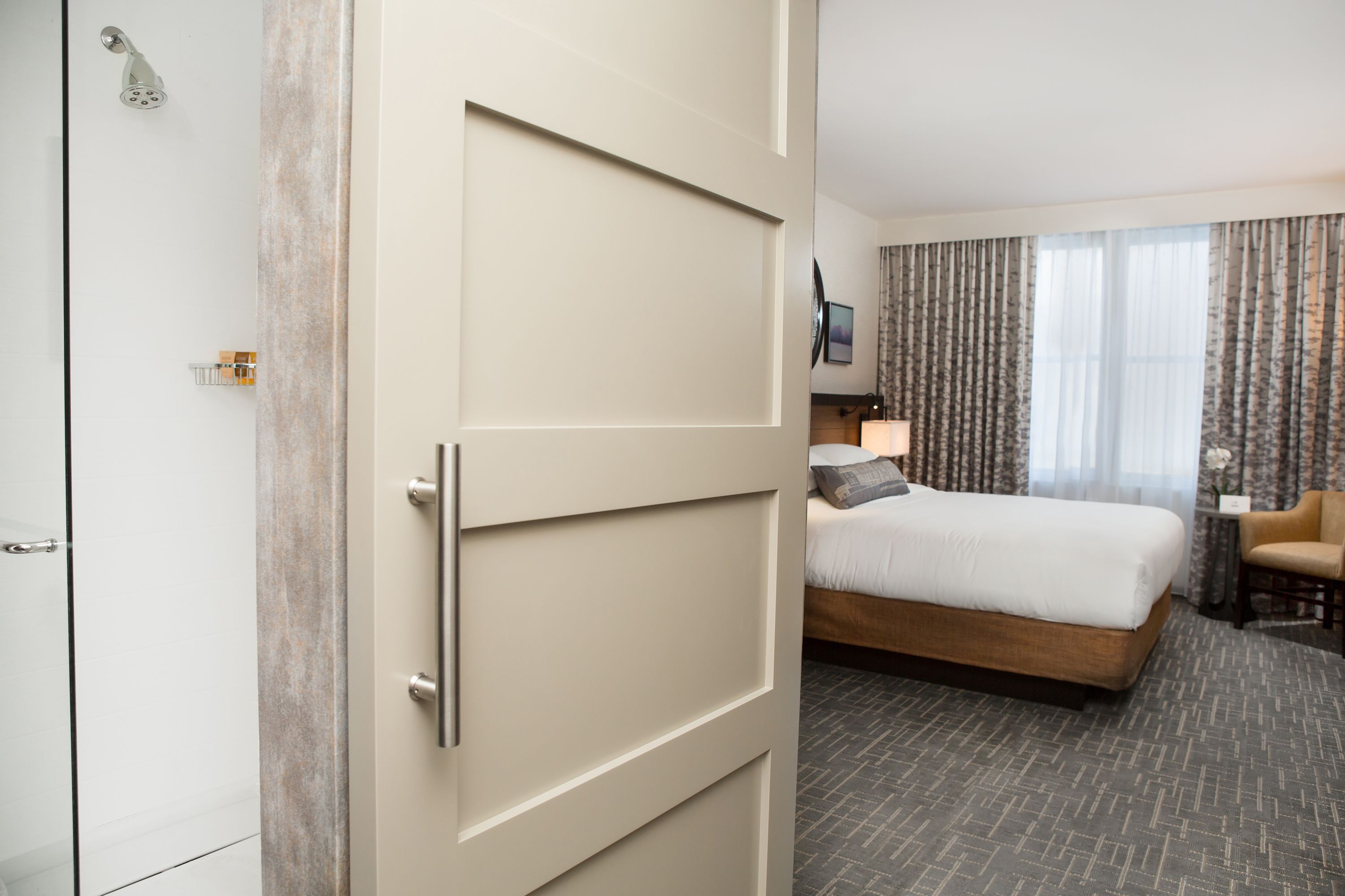 A hotel room with a bed, a chair, a desk, and a shower.