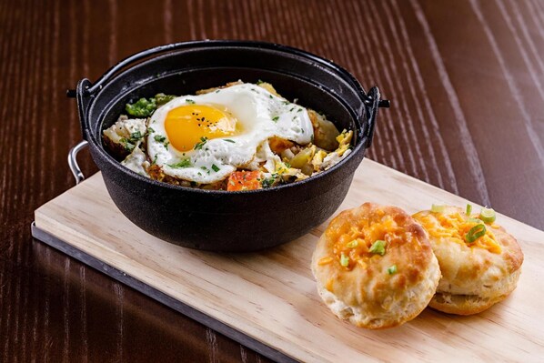 A black cast iron skillet with a fried egg and hash browns on a wooden board.