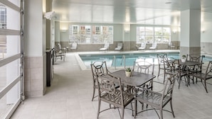An indoor pool area with seating and tables, large windows, and a view of the outside. - Hotel Madison & Shenandoah Conference Ctr (Harrisonburg)