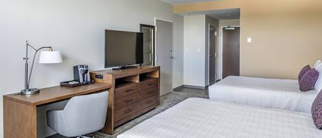 A hotel room with a wooden desk, a chair, a bed with white bedding, and a television.