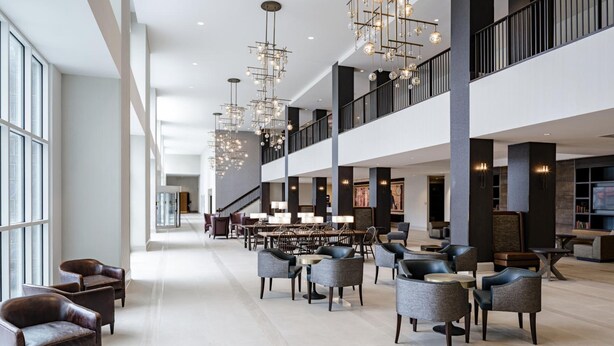 A spacious lobby with high ceilings, modern chandeliers, and a variety of seating options including leather armchairs and sofas. - Hotel Madison & Shenandoah Conference Ctr (Harrisonburg)