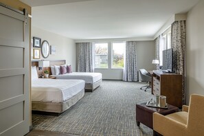A hotel room with two beds, a desk, a chair, a TV, and a window with curtains.