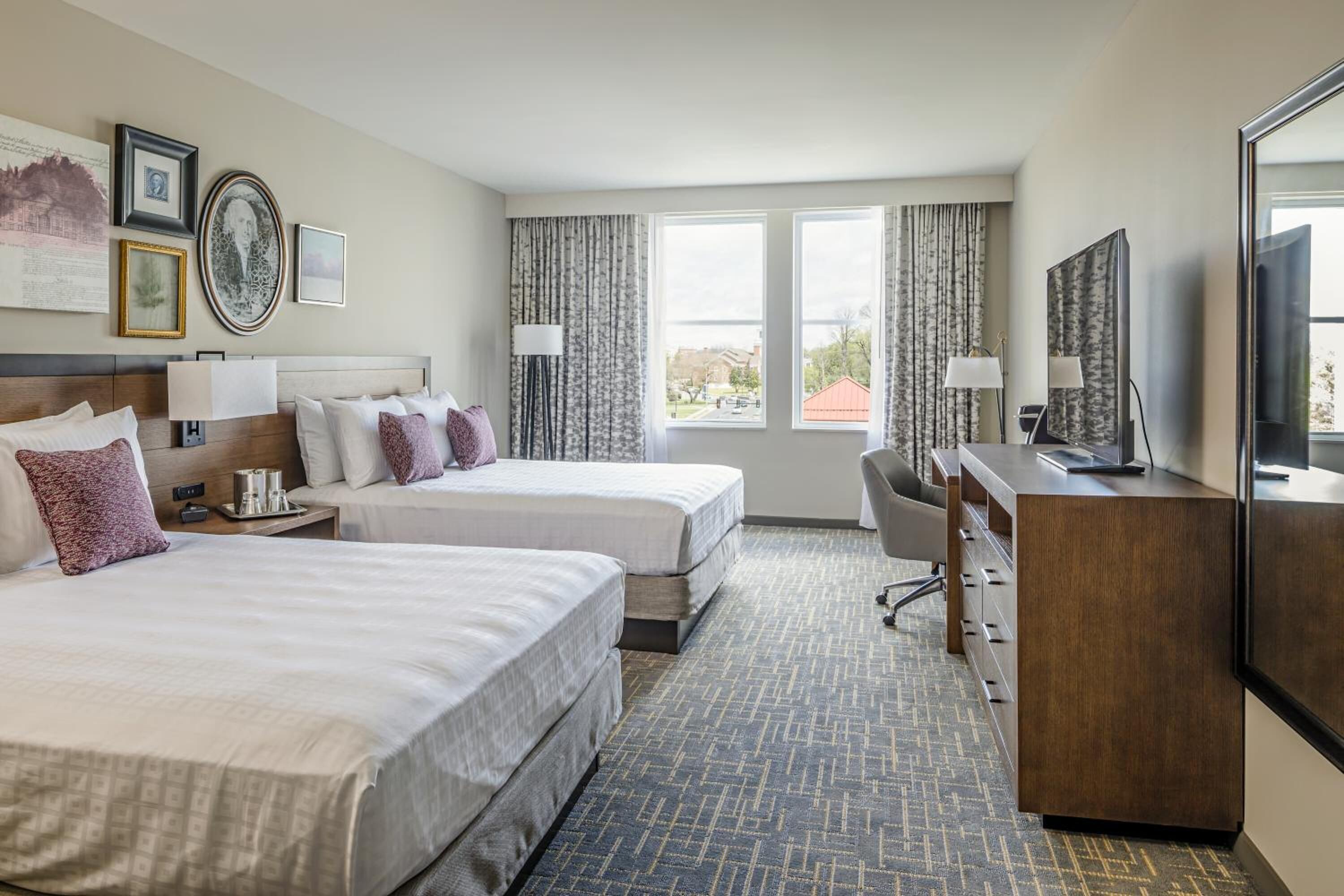 A hotel room with two beds, a desk, a chair, and a TV.