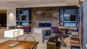 A modern living room with a fireplace, comfortable seating, a TV, and a bookshelf. - Hotel Madison & Shenandoah Conference Ctr (Harrisonburg)