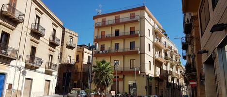 Un edificio residencial de varios pisos con balcones, una palmera y coches aparcados.