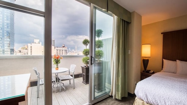 A hotel room with a balcony, a bed, a table with chairs, and a view of the cityscape.