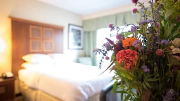 A hotel room with a neatly made bed, a bedside table, and a floral arrangement on the nightstand.