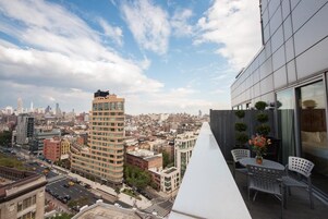 A high-rise building with a terrace featuring outdoor seating and a city view.