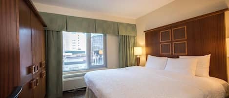 Habitación de hotel con una cama grande, un armario, una ventana con cortinas y vistas a edificios.