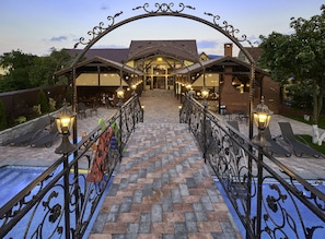 A hotel entrance with a brick pathway leading to a covered area with outdoor seating. - Resort Ambient (Cristian)