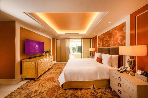 A hotel room with a bed, a television, a desk with a lamp, and a view of the outdoors. - Okada Manila (ParaƱaque)