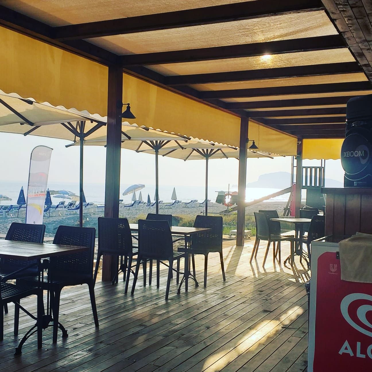 An outdoor seating area with tables and chairs, umbrellas, and a view of the beach.