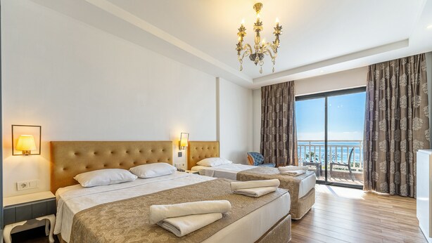 A hotel room with two beds, a chandelier, a balcony with curtains, and a view of the sea. - Sey Beach Hotel & Spa (Alanya)