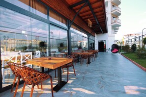 An outdoor seating area with tables and chairs, large windows, and a view of the surrounding buildings. - Sey Beach Hotel & Spa (Alanya)