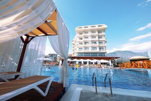 A swimming pool area with lounge chairs and umbrellas, a poolside deck, and a multi-story building in the background. - Sey Beach Hotel & Spa (Alanya)