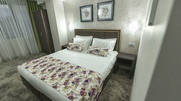 Un cuarto de hotel ordenado con una cama grande, una mesita de noche, un armario y dos cuadros con flores en la pared.