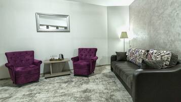 Una sala de estar con un sofá gris, dos sillones morados, una mesita y una lámpara.