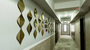 A hallway with a series of diamond-shaped mirrors on the wall, a carpeted floor, and doors leading to rooms.
