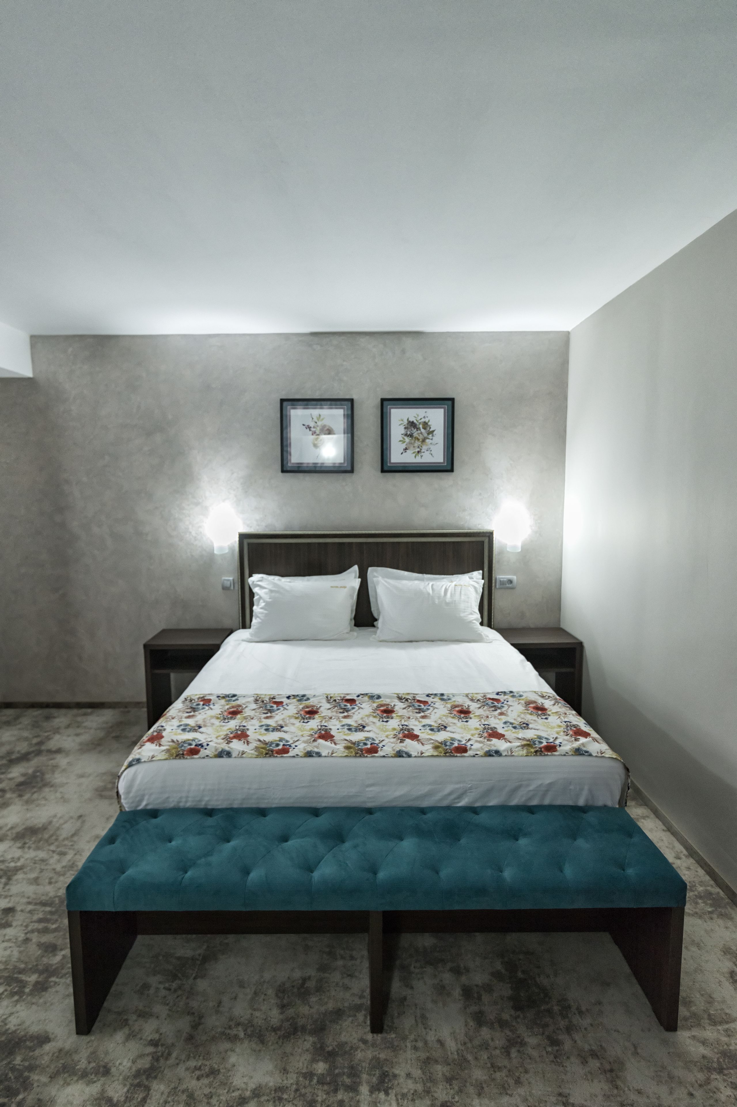 A bedroom with a bed, two bedside tables, a bench, and two wall-mounted lights.