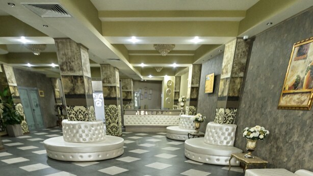 Een hotellobby met een zwart-wit schakerend vloerkleed, een centraal zitgedeelte met banken, en een receptiebalie.