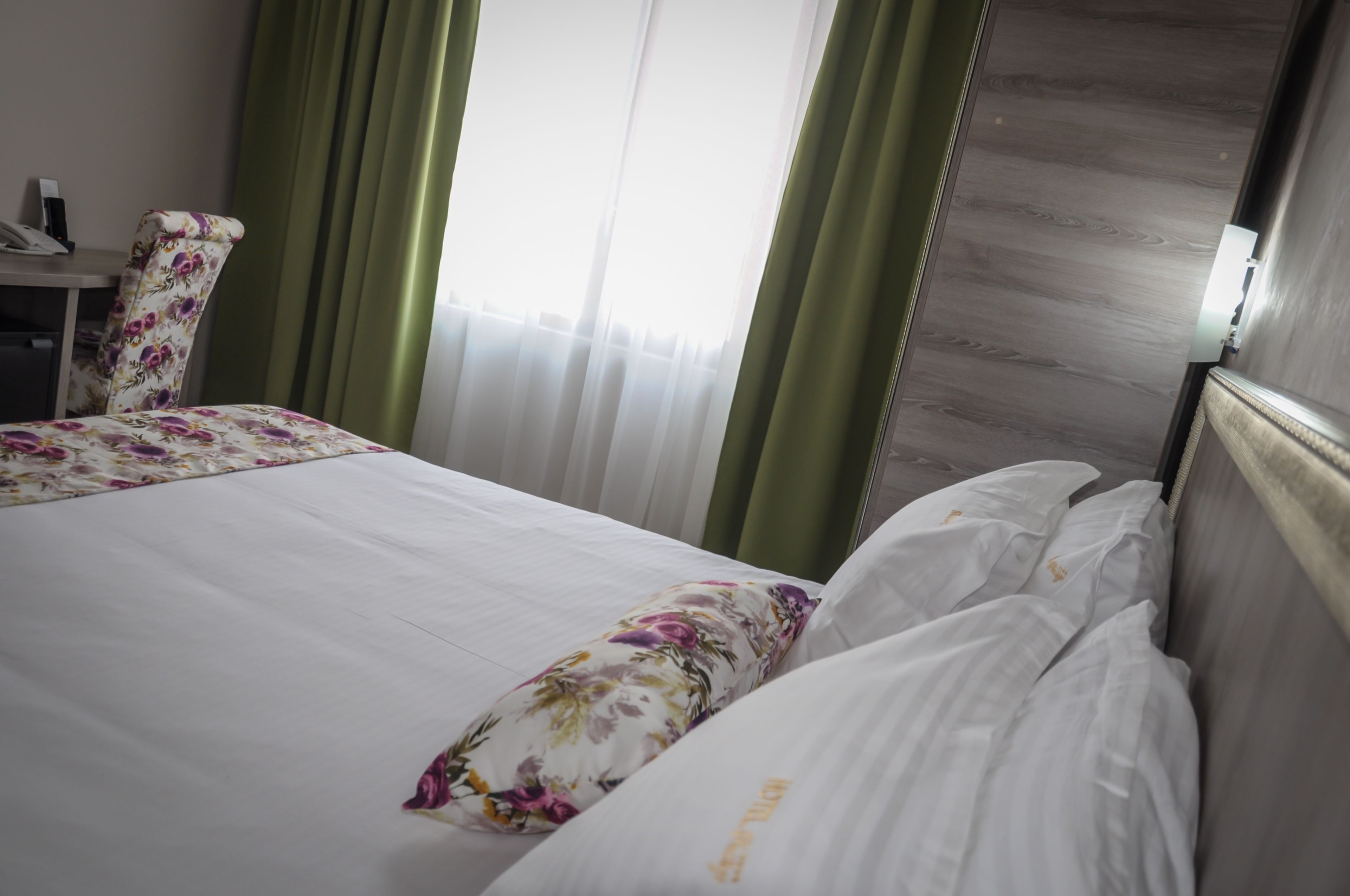 A hotel room with a bed, a chair, and a desk with a telephone.
