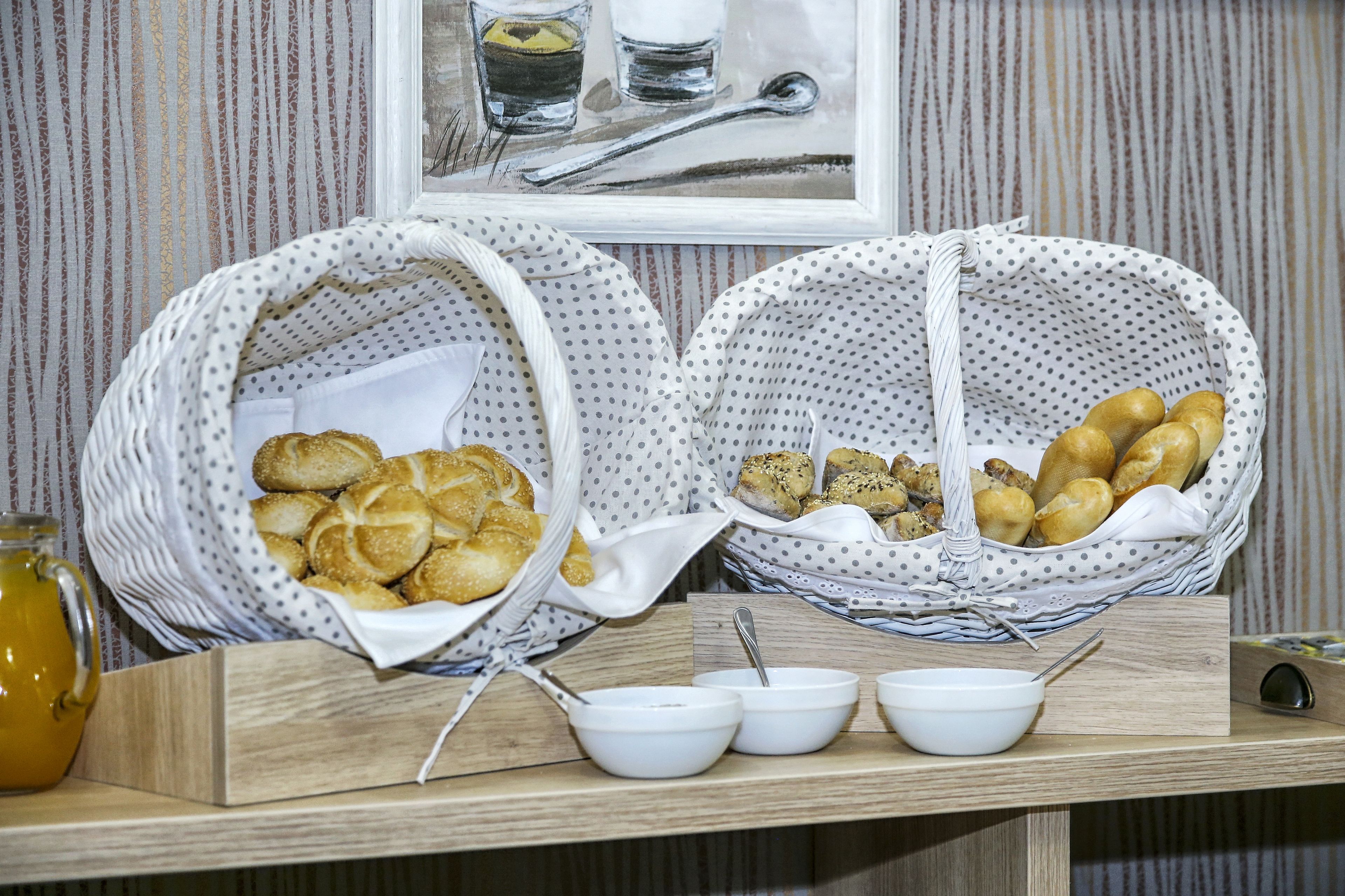 A breakfast buffet with bread baskets and bowls of food on a wooden table.