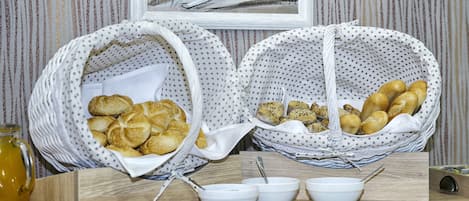 A breakfast buffet with bread baskets and bowls of food on a wooden table.